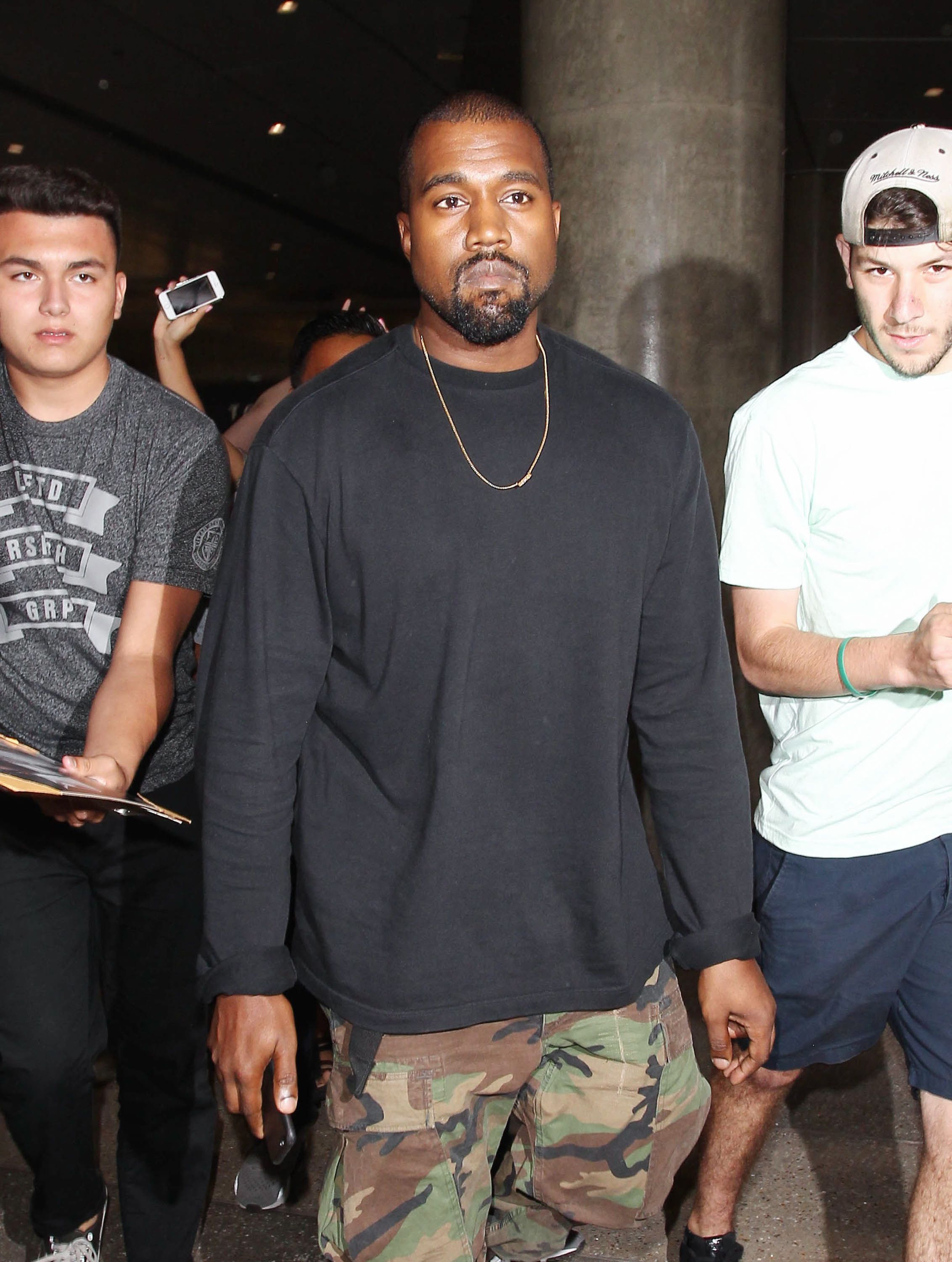 07/01/2015 - Kanye West - Kanye West Sighted at LAX Airport on July 1, 2015 - Los Angeles International Airport - Los Angeles, CA, USA - Keywords: 3/4 Length Shot, Smartphone, iPhone 6, Camo Pants, Brown and Green Camouflage Pants, Blue Long Sleeve Shirt, Gold Pendant, Facial Hair, Beard, Goatee, Person, Man, Vertical, Candid, Gold Necklace, Jewelry, Vertical, Casual Fashion, Travel, California, Arts Culture and Entertainment, Celebrities, Celebrity, Walking, Singer, Performer, Rapper Orientation: Portrait Face Count: 1 - False - Photo Credit: STPR / PRPhotos.com - Contact (1-866-551-7827) - Portrait Face Count: 1